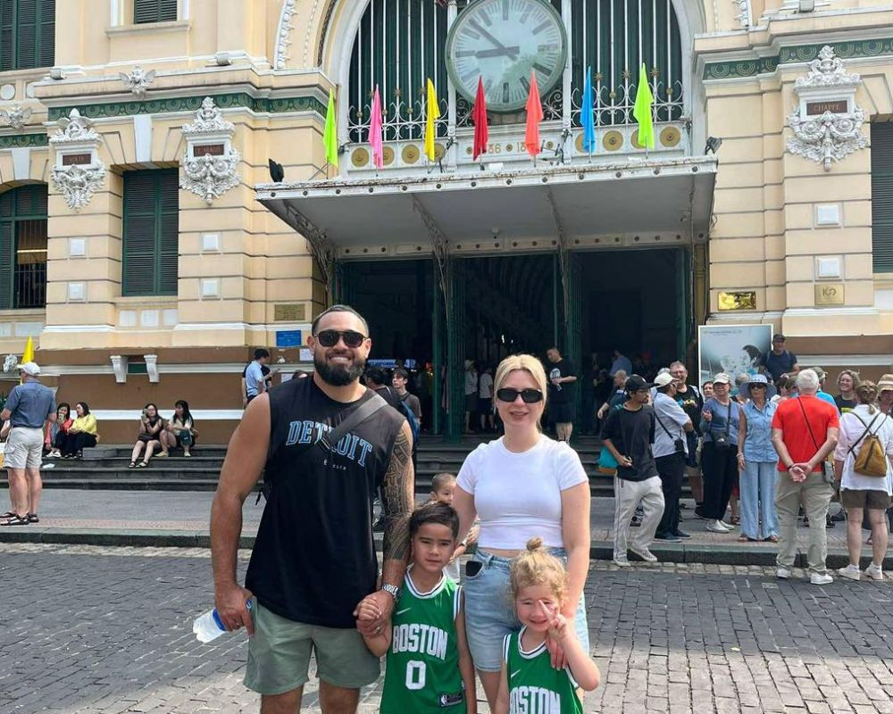 Family of four smiling in front of Saigon Central Post Office