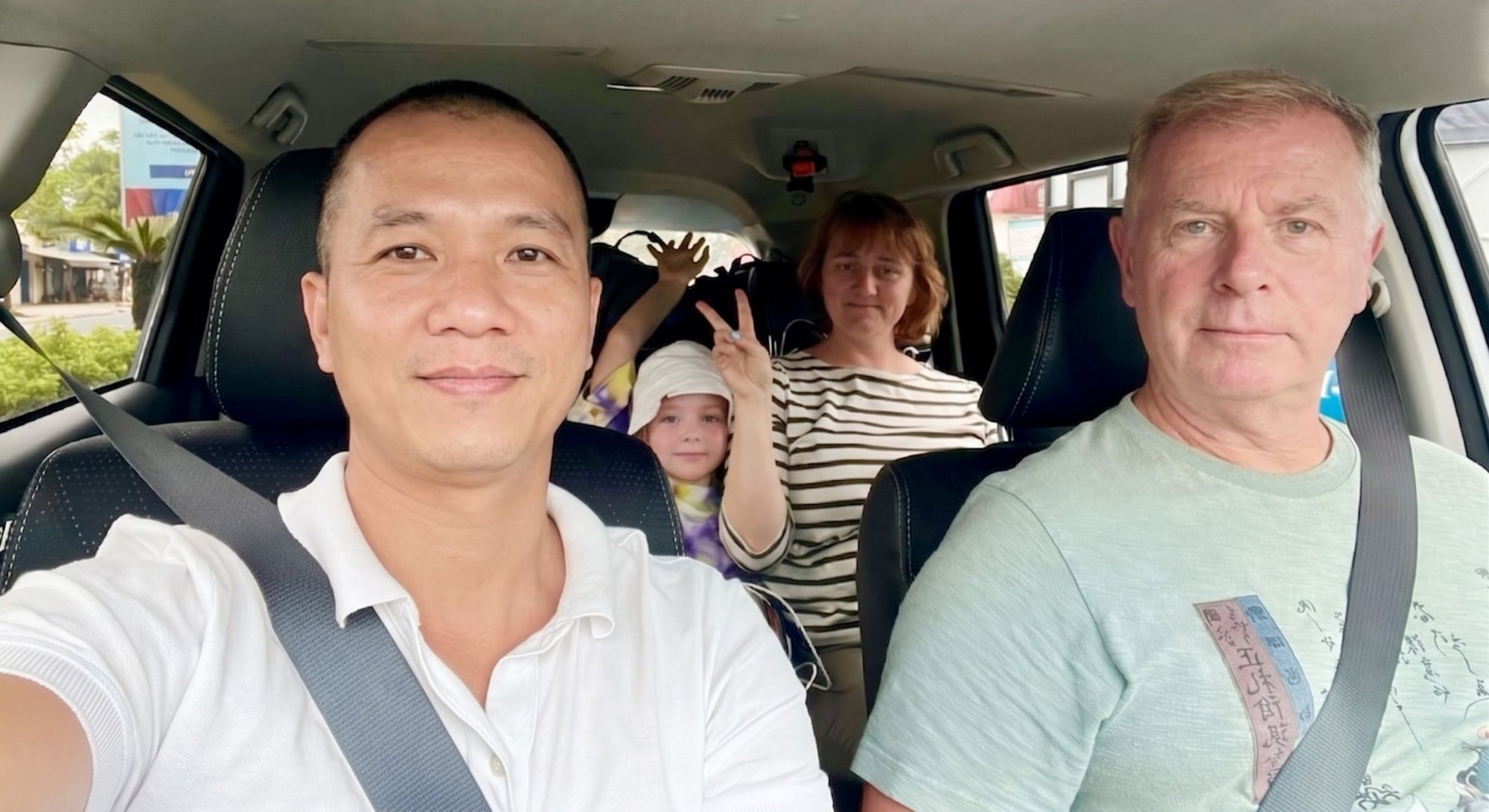 Friendly-local-driver-taking-a-selfie-with-a-happy-foreign-tourist-family-inside-a-private-transfer-car