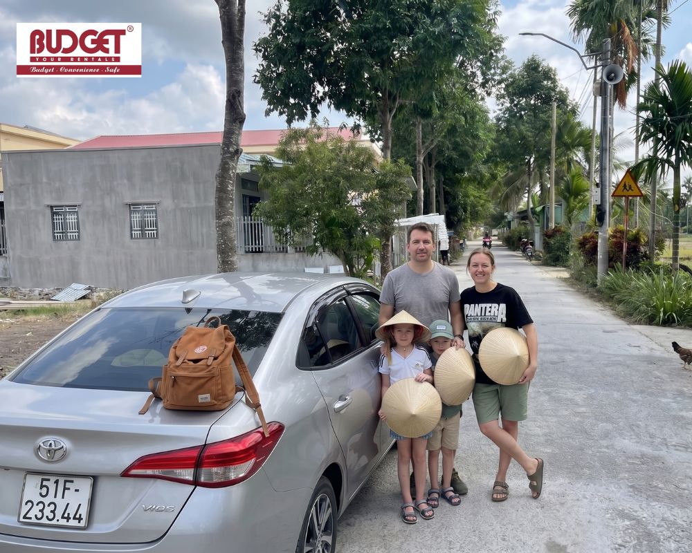 Foreign-family-wearing-traditional-conical-hats-standing-by-a-silver-Toyota-Vios-car-on-My-Tho-and-Ben-Tre-tour