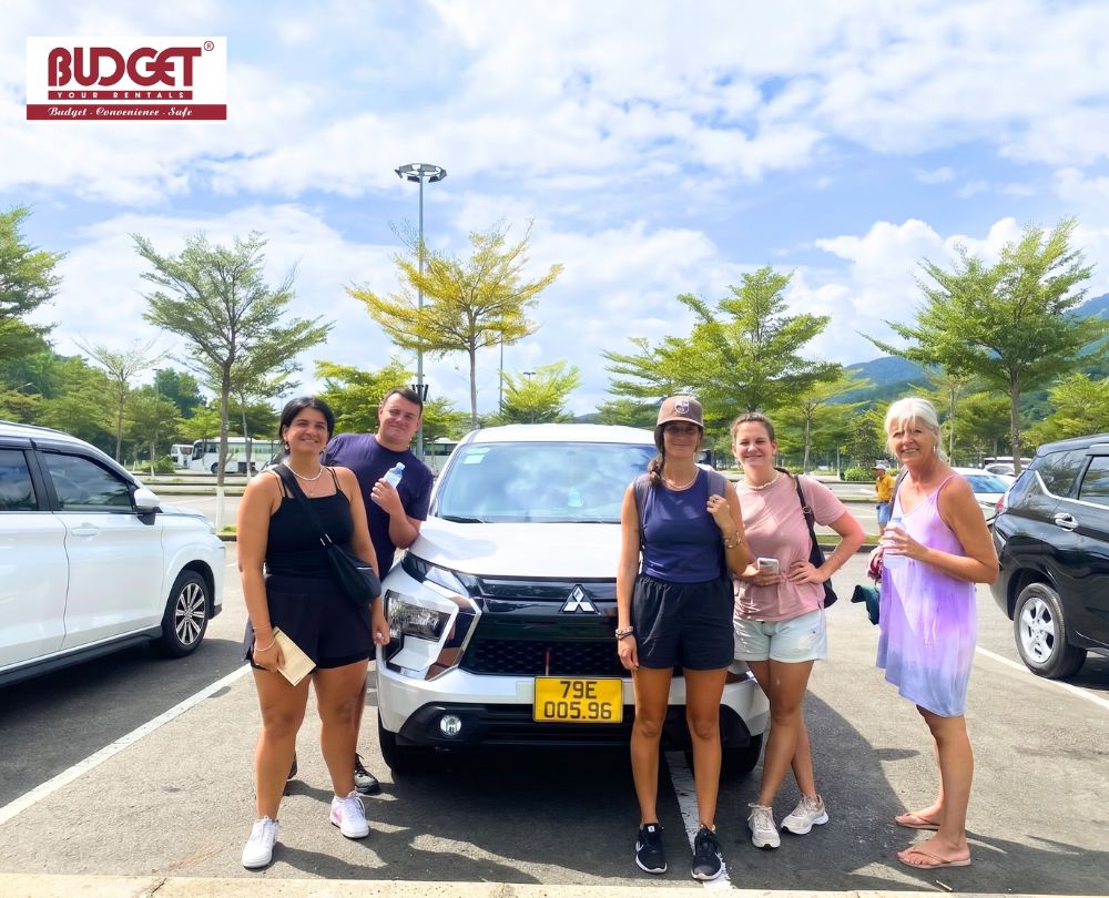 Group-of-5-foreign-tourists-posing-next-to-our-white-Mitsubishi-Xpander-rental-car-in-a-Nha-Trang-parking-lot