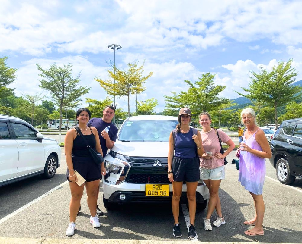 Group-of-five-foreign-tourists-posing-next-to-their-white-Mitsubishi-Xpander-rental-car-in-a-Nha-Trang-parking-lot