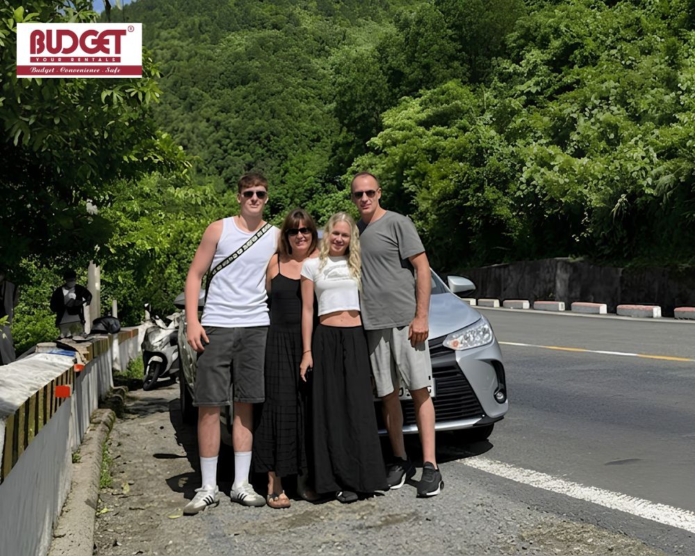 Group-of-tourists-posing-beside-a-silver-Toyota-Vios-sedan-on-a-scenic-mountain-road-in-Sapa