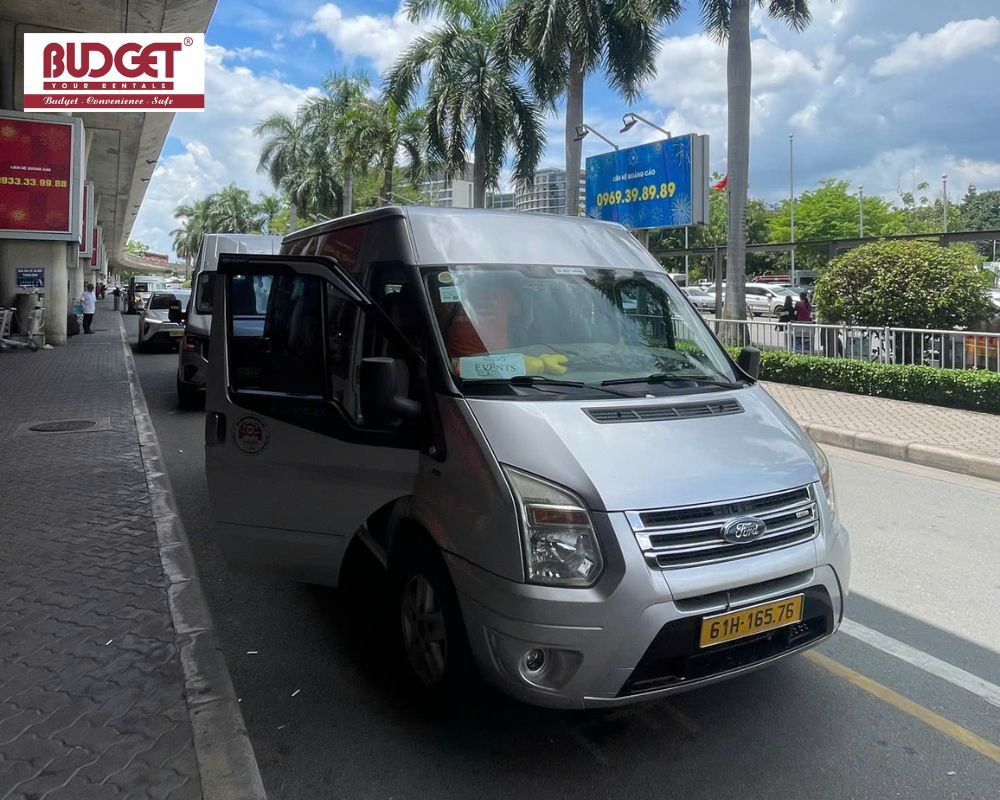 Silver-16-seat-Ford-Transit-van-waiting-at-the-airport-pickup-lane-for-a-private-group-transfer-service