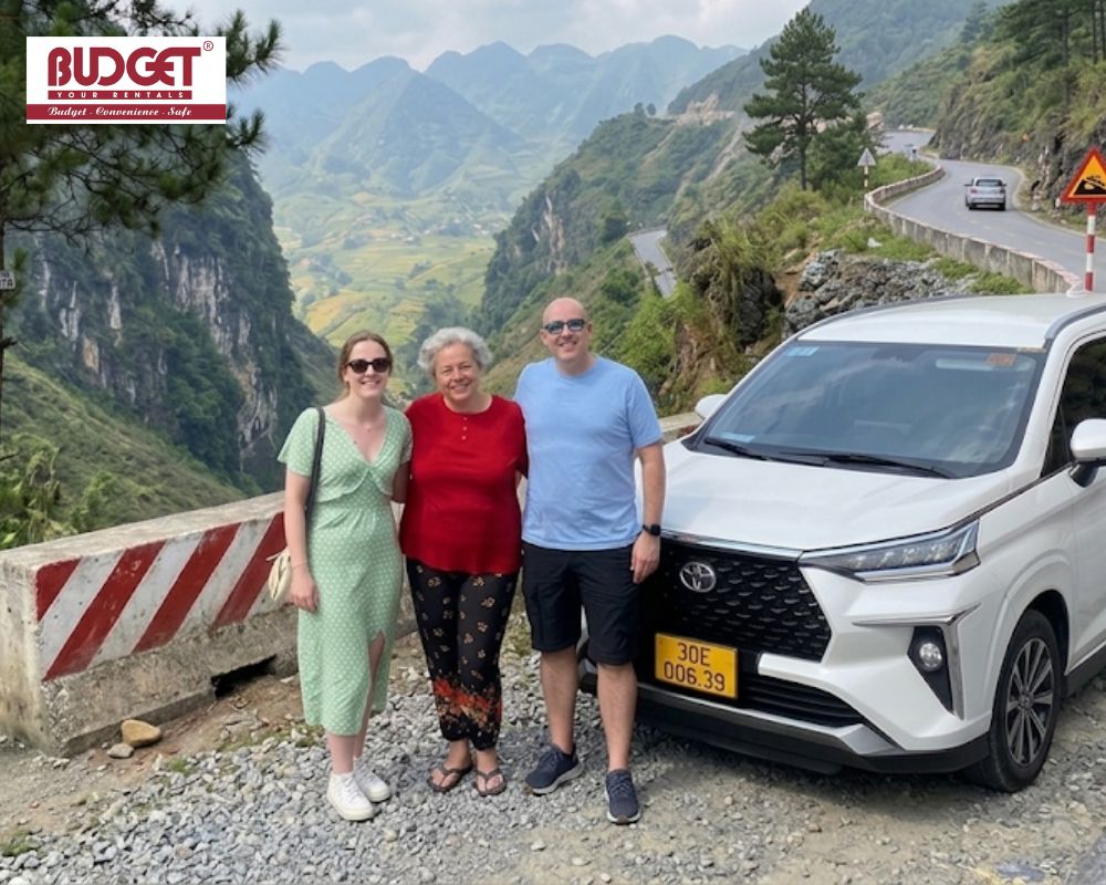 Three-foreign-tourists-posing-next-to-a-white-Toyota-SUV-on-a-spectacular-mountain-pass-in-Ha-Giang