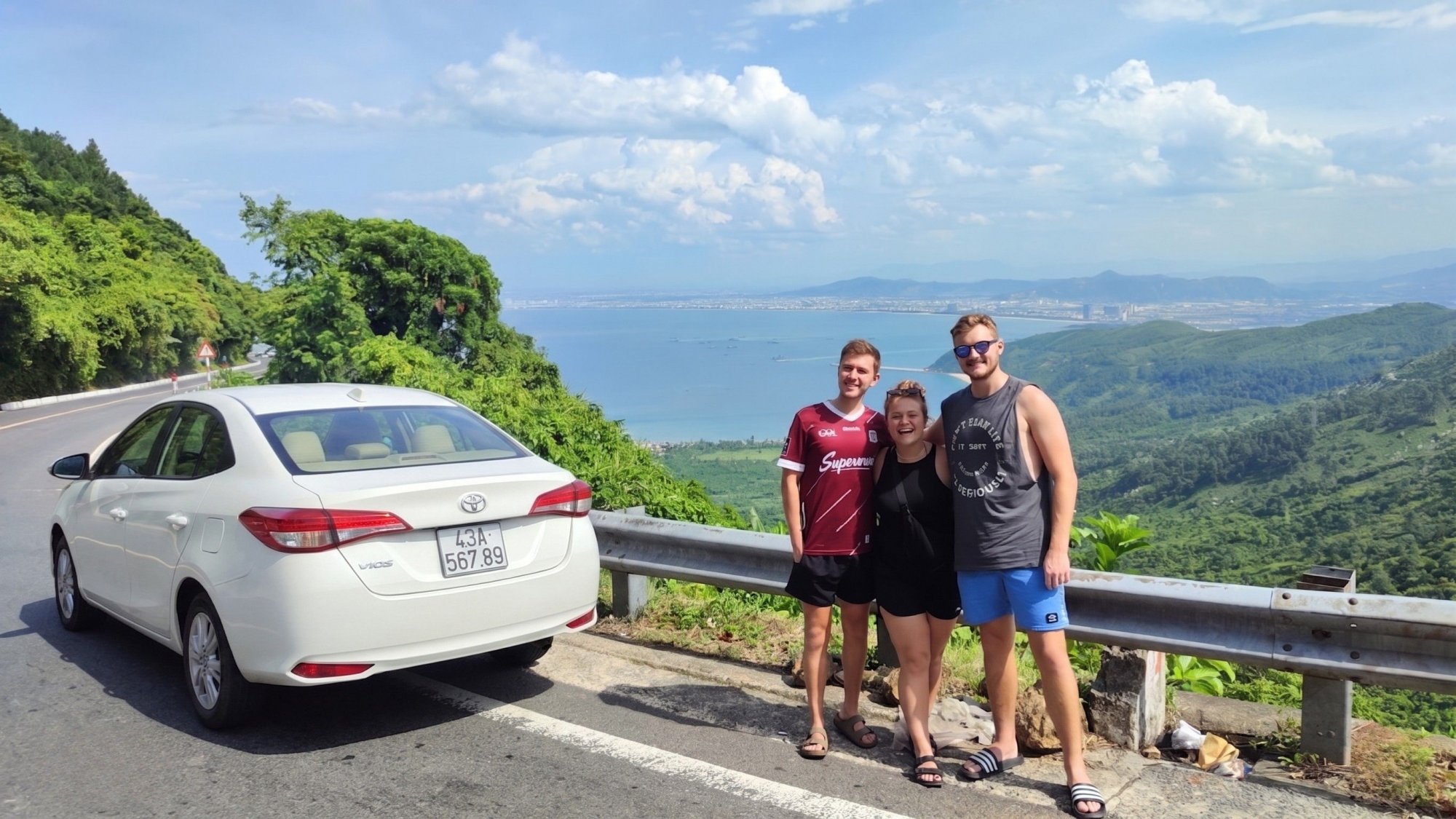 Three-foreign-tourists-posing-with-our-white-4-seater-private-car-on-the-scenic-Hai-Van-Pass-overlooking-the-ocean