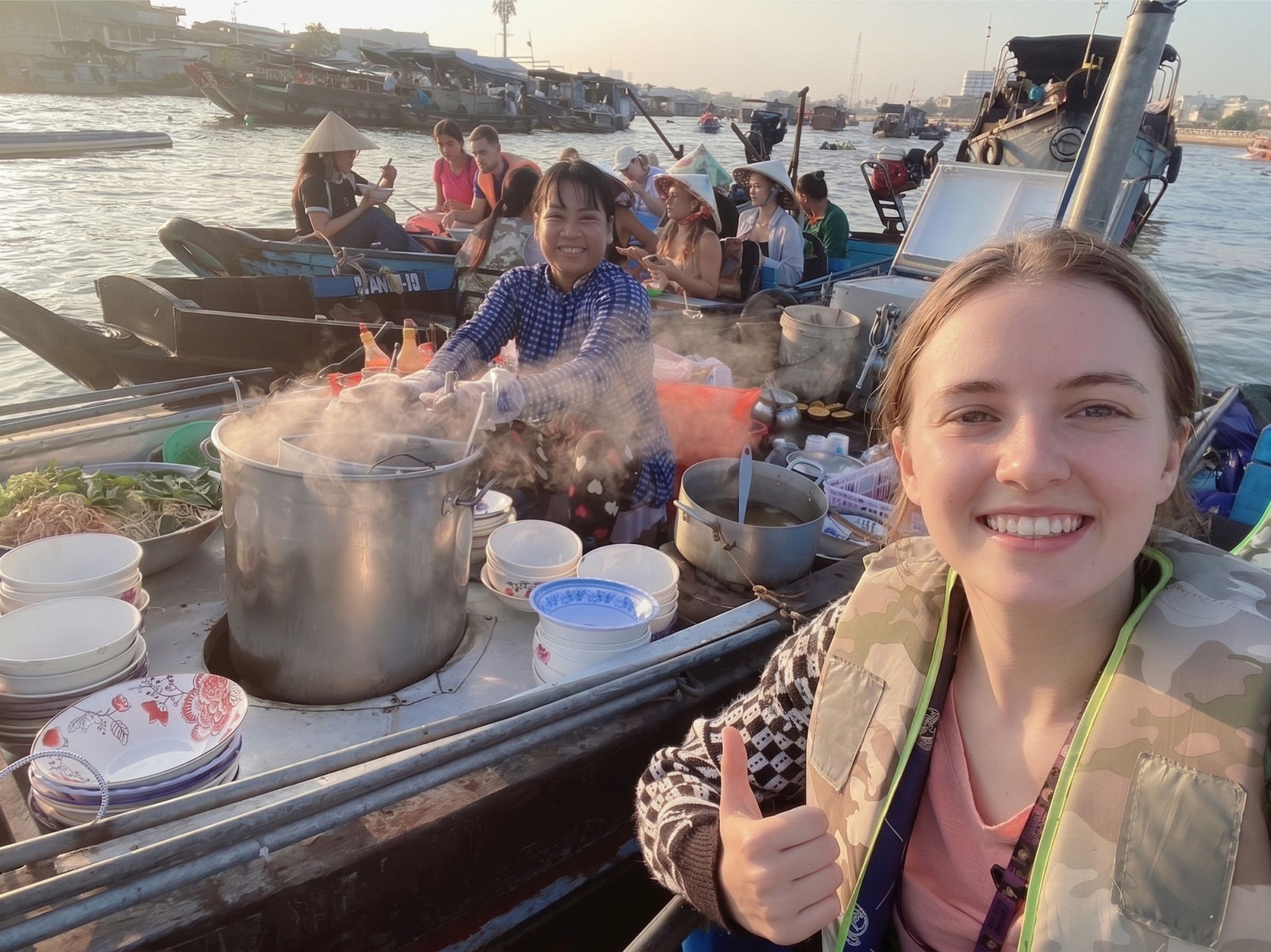 Tourist-taking-a-selfie-on-a-wooden-boat-while-a-local-vendor-prepares-a-hot-bowl-of-Bun-Rieu-at-Cai-Rang-floating-market