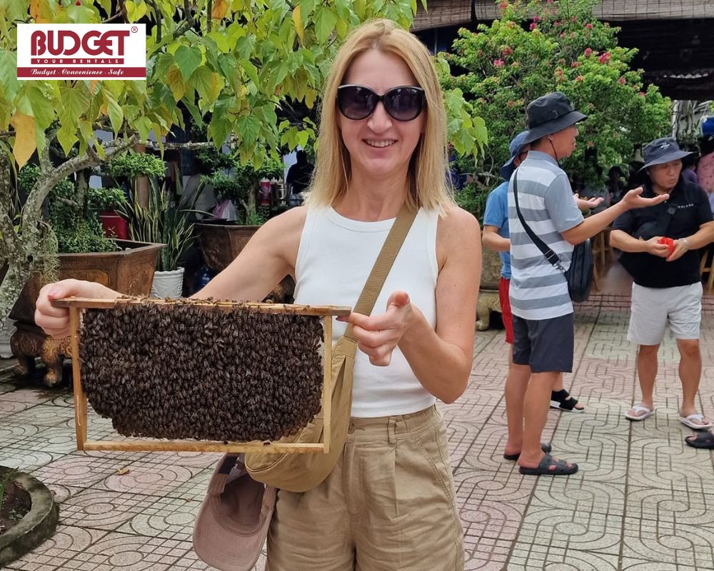 A-female-visitor-holding-a-frame-covered-in-honeybees-at-a-local-bee-farm-in-the-Mekong-Delta