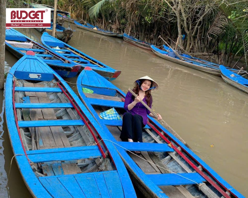 A-woman-tourist-wearing-a-conical-hat-rowing-a-traditional-wooden-sampan-boat-along-the-water-canals-in-Ben-Tre