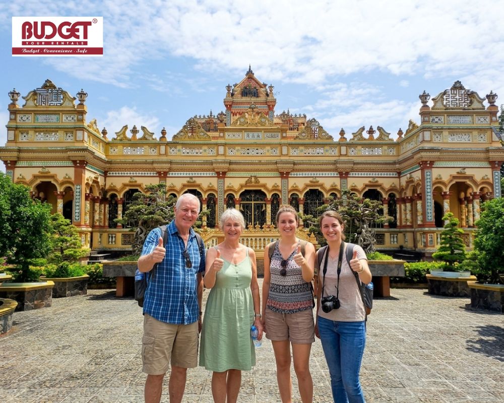 Four-international-travelers-gave-thumbs-up-while-tajing-a-photo-in-front-of-the-ornate-architecture-of-Vinh-Trang-Pagoda