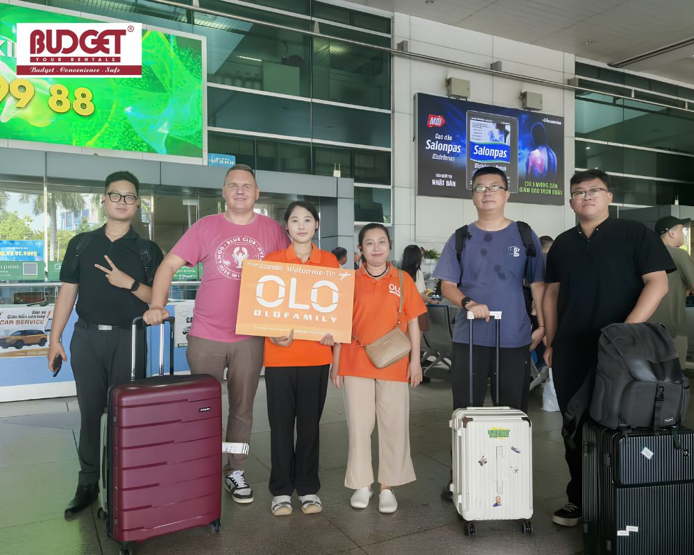 Happy-group-of-tourists-and-local-guides-posing-with-their-luggage-and-a-welcome-sign-upon-arrival-at-the-airport-terminal