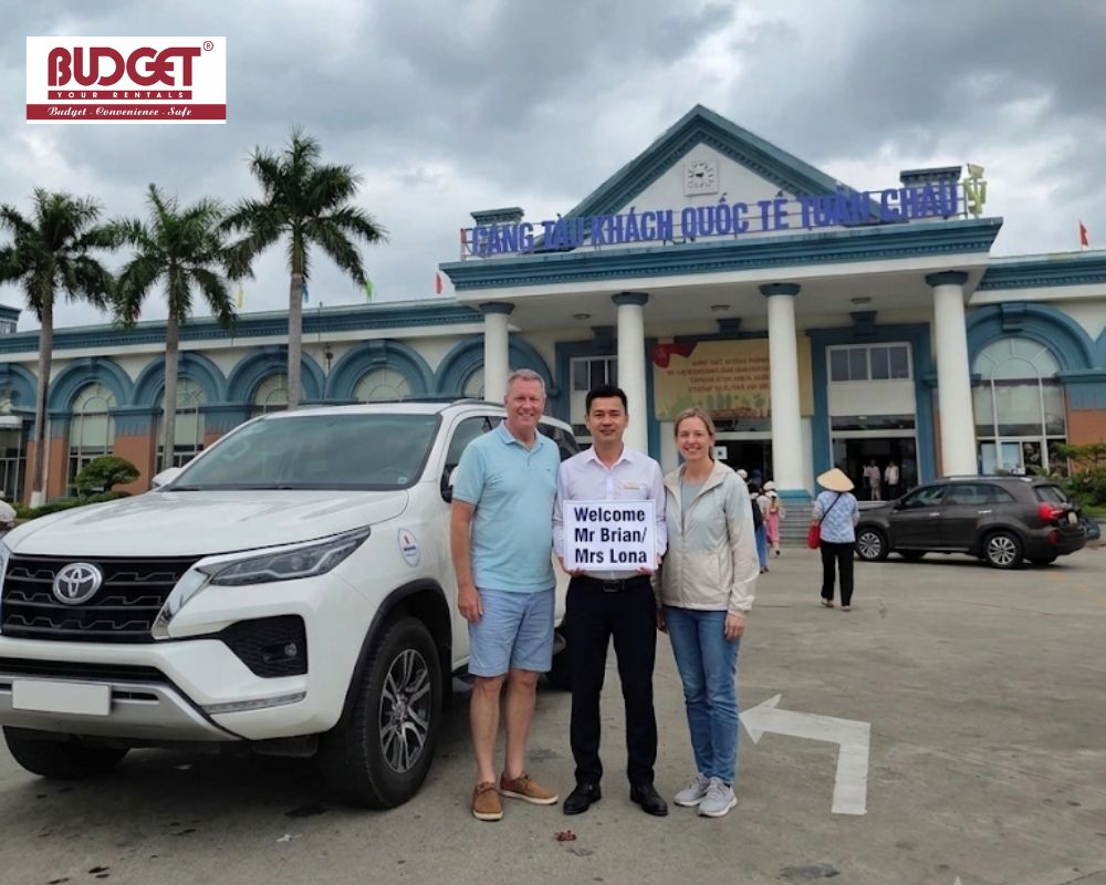 Our-driver-and-the-couple-took-a-photo-with-a-welcome-sign-next-to-our-7-seat-car-outside-Tuan-Chau-Port-in-Ha-Long