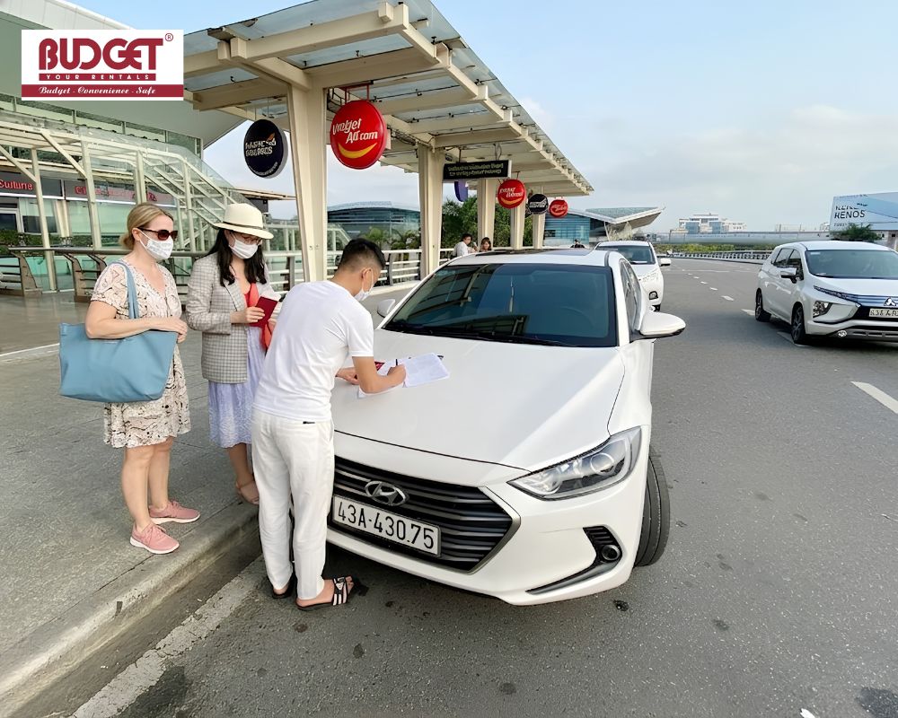 Our-driver-assisting-female-tourists-with-rental-agreement-paperwork-on-the-hood-of-a-white-Hyundai-sedan-at-Phu-Cat-airport