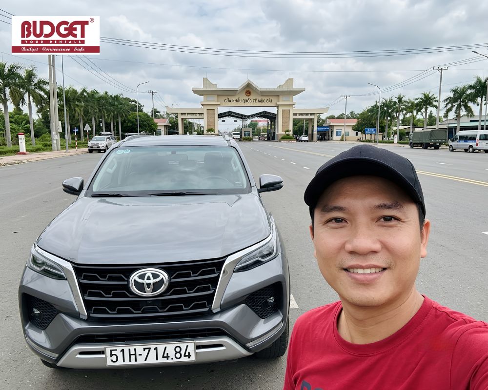 Our-driver-taking-a-selfie-next-to-a-modern-grey-Toyota-SUV-at-the-Moc-Bai-International-Border-Gate-in-Tay-Ninh
