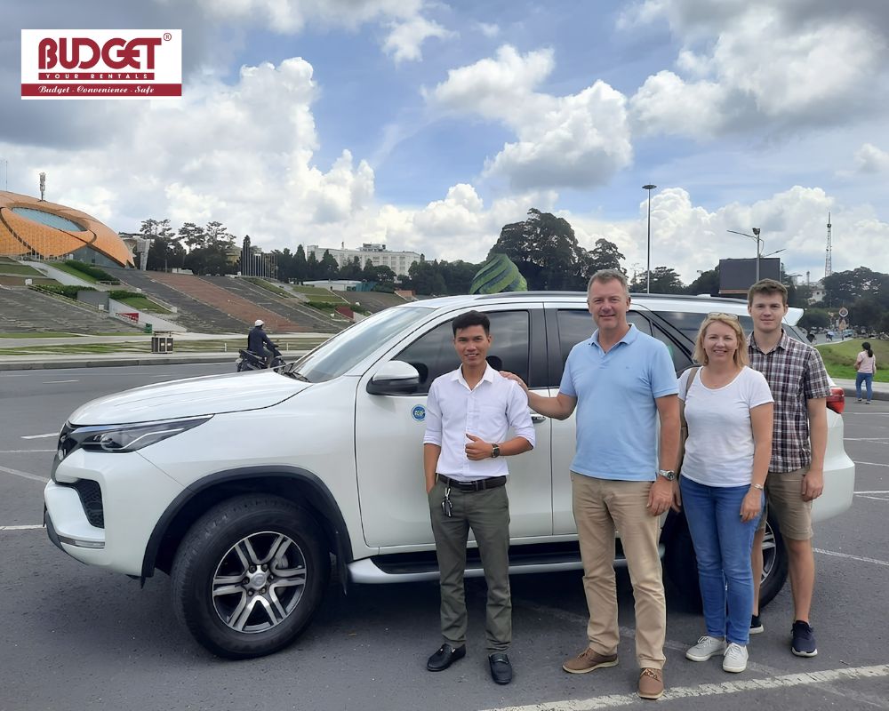 Smiling-family-posing-alongside-our-driver-and-a-white-SUV-at-Lam-Vien-Square-before-starting-their-trip-down-to-Nha-Trang