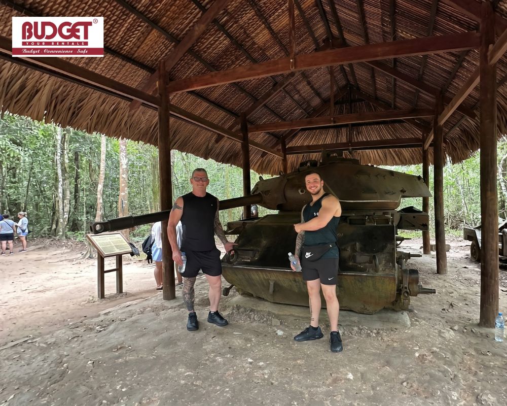 Visitors-standing-next-to-a-historic-rusted-military-tank-preserved-under-a-thatched-shelter-at-the-Cu-Chi-Tunnels