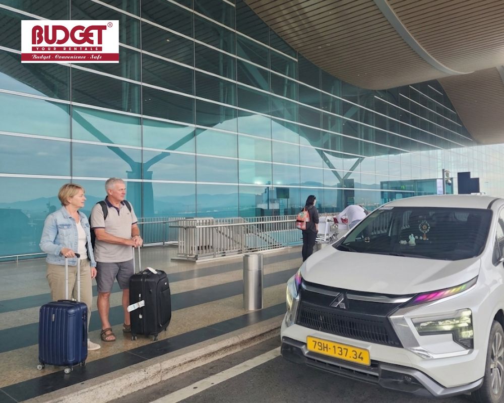 Two-French-people-with-their-luggage-are-standing-next-to-our-white-rental-car-outside-the-airport-terminal