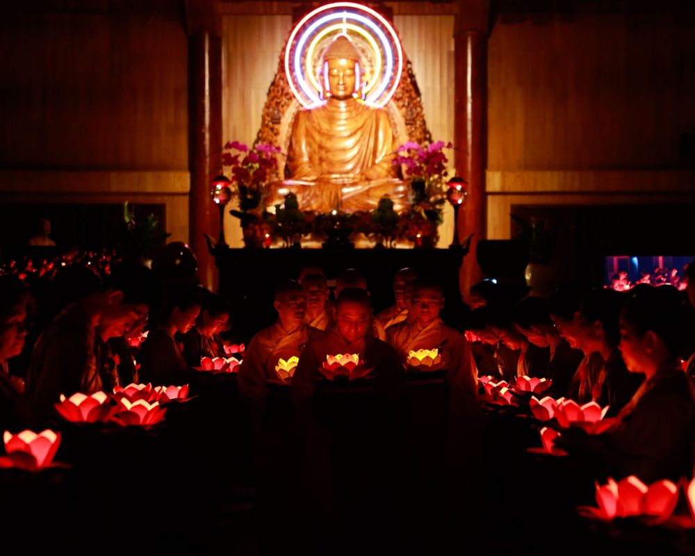 Devotees gather for a solemn candle-lit ceremony in front of a Buddha statue