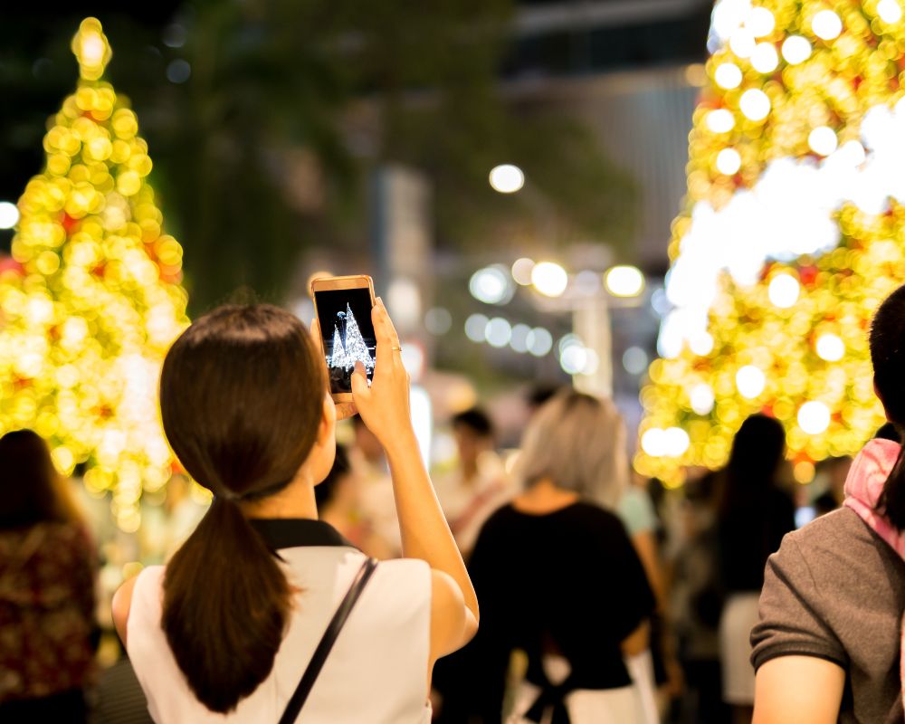 Woman hand holding mobile phone take a photo of christmas tree